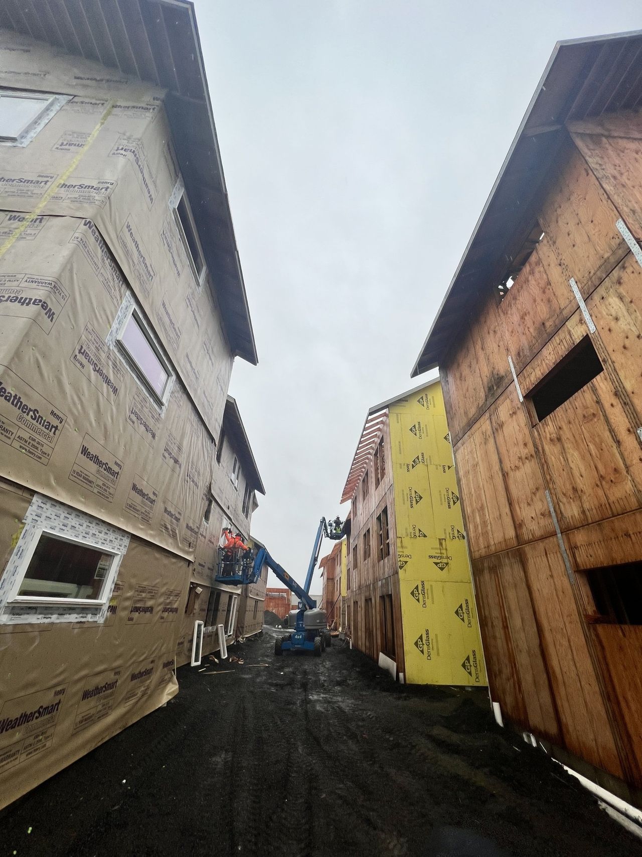A man is standing on a lift between two buildings under construction.