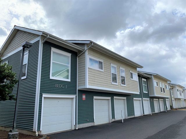 A row of apartment buildings with green siding and white garage doors.