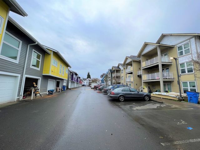 A row of apartment buildings with cars parked on the side of the road.