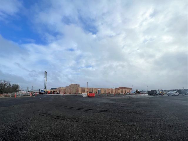 A large building is being built on a cloudy day in a parking lot.