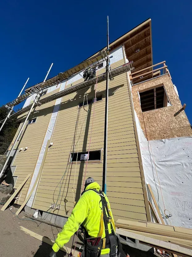 A man in a yellow jacket is standing in front of a building under construction.