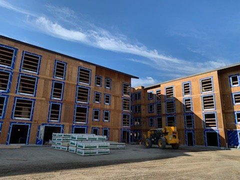 A large apartment building under construction with a bulldozer parked in front of it.