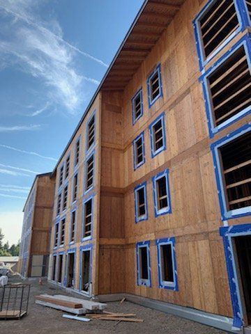 A large wooden building under construction with blue tape on the windows.