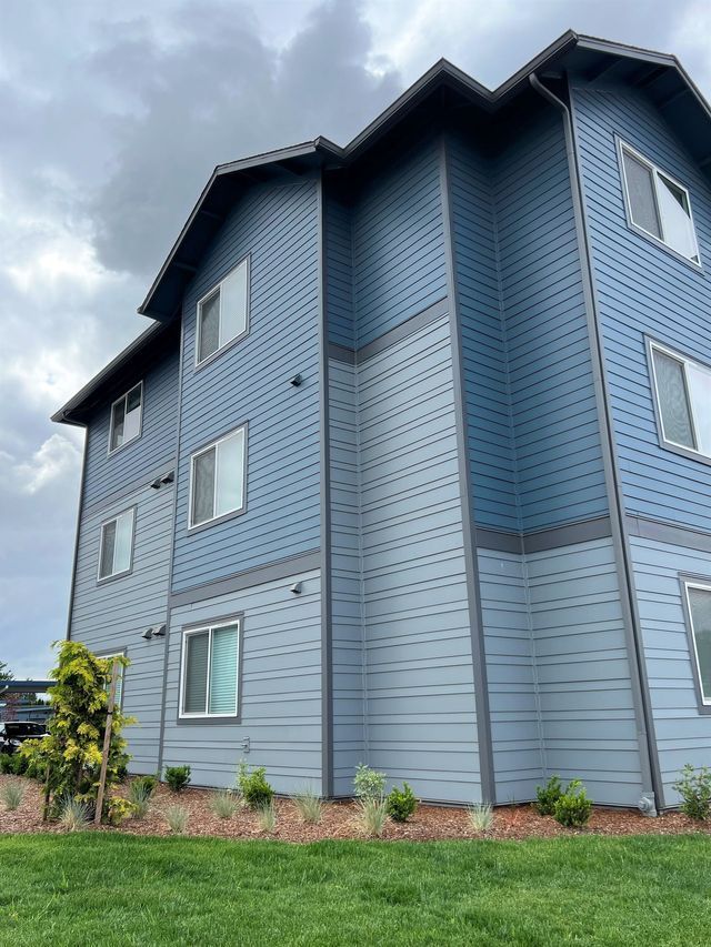A large blue apartment building with a lot of windows is sitting on top of a lush green lawn.