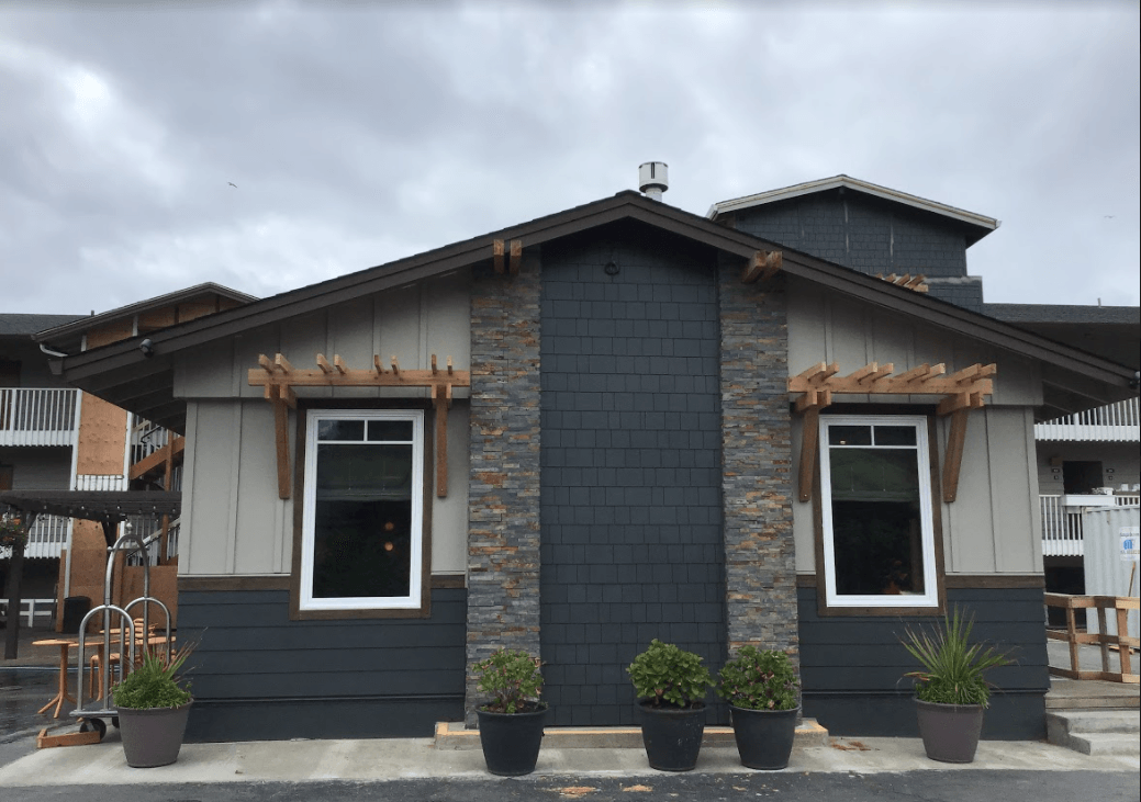 A small house with a lot of windows and potted plants in front of it.