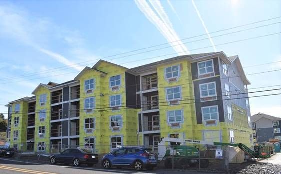 A large apartment building under construction with cars parked in front of it.