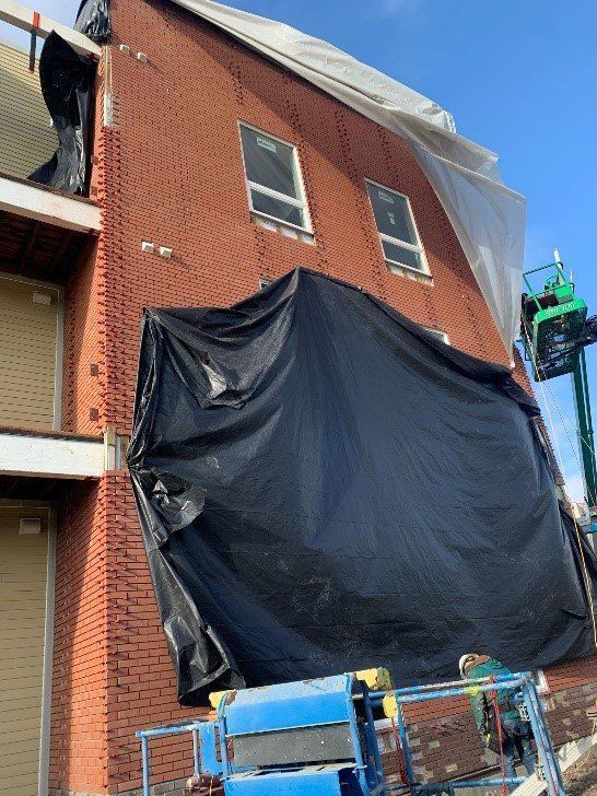 A large brick building is being covered with a black tarp.