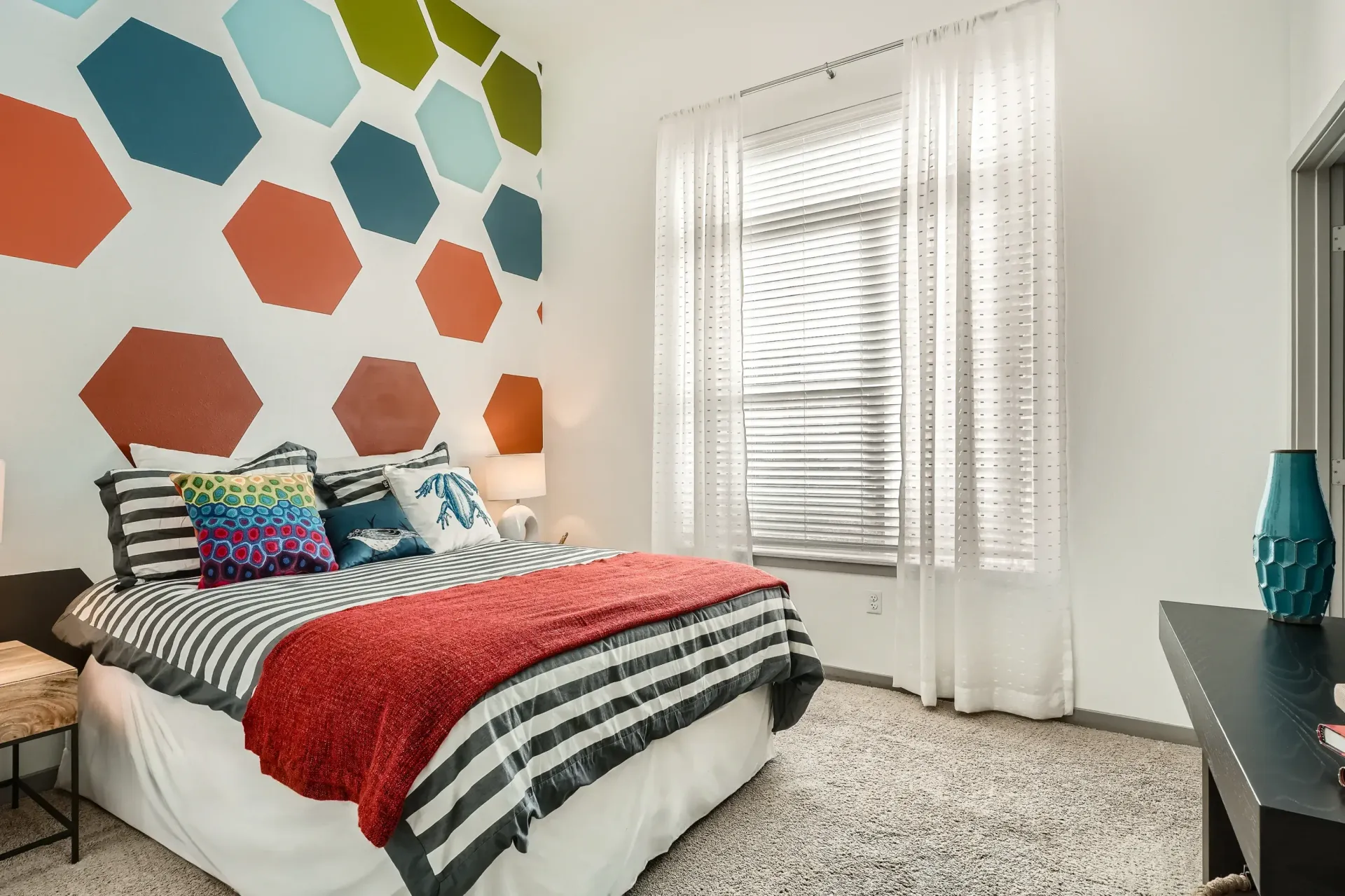 Bedroom with a bold hexagon wall mural, striped bedding, and white sheer curtains.