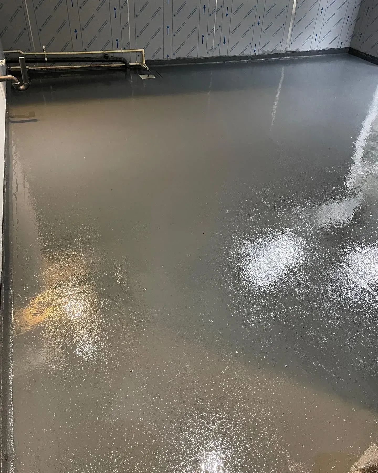 Glossy gray floor in a mostly empty room, with a bench against the wall and bright reflections on the surface