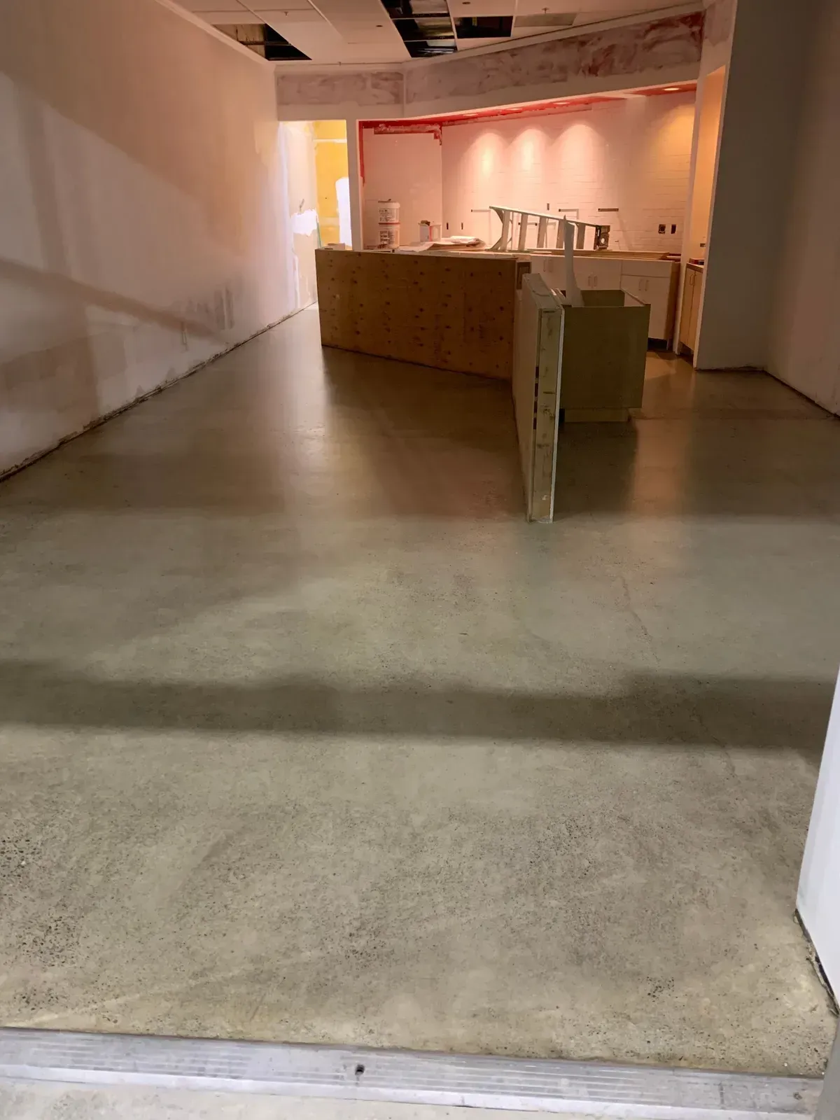 Concrete floor leads to a counter in a room under construction with white walls.
