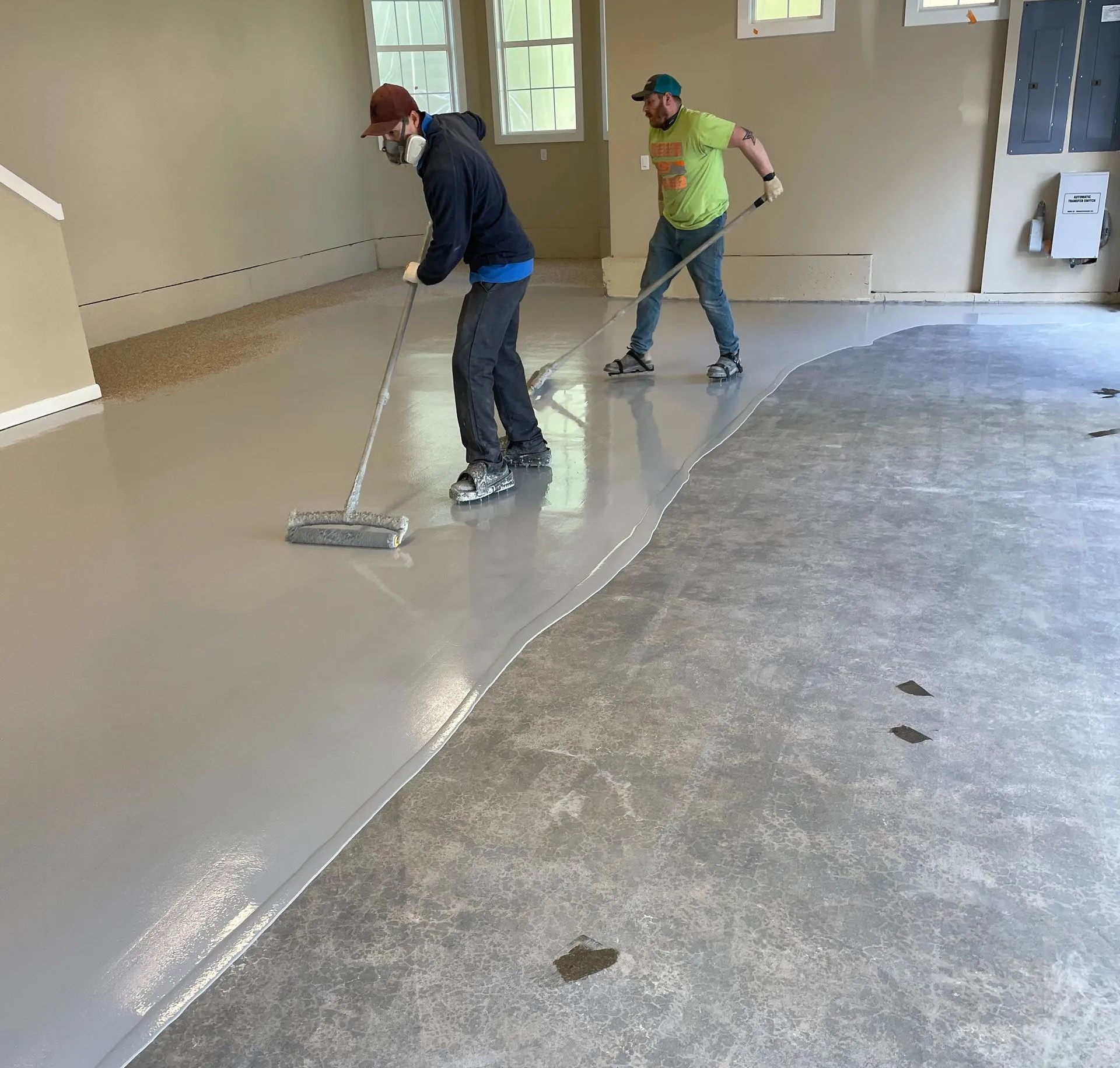 Two workers smoothing a light gray floor in a room under construction.
