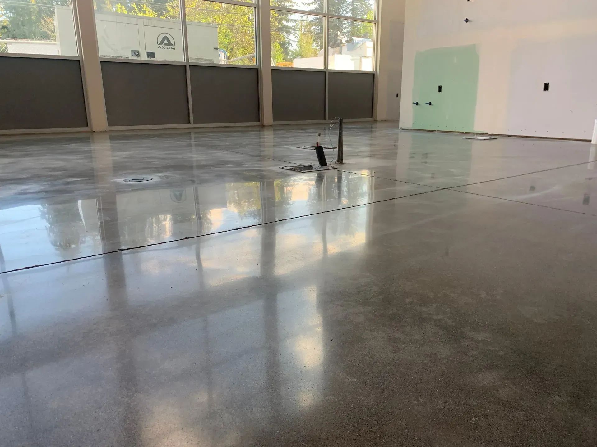 Empty polished indoor room with large windows, wet reflective floor, and exposed pipes in the center