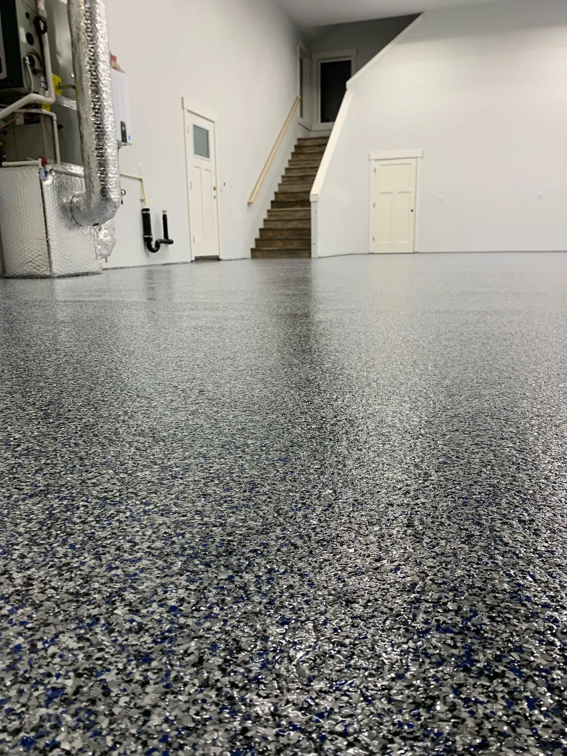 Garage with a speckled epoxy floor, white walls, and a staircase leading upstairs.