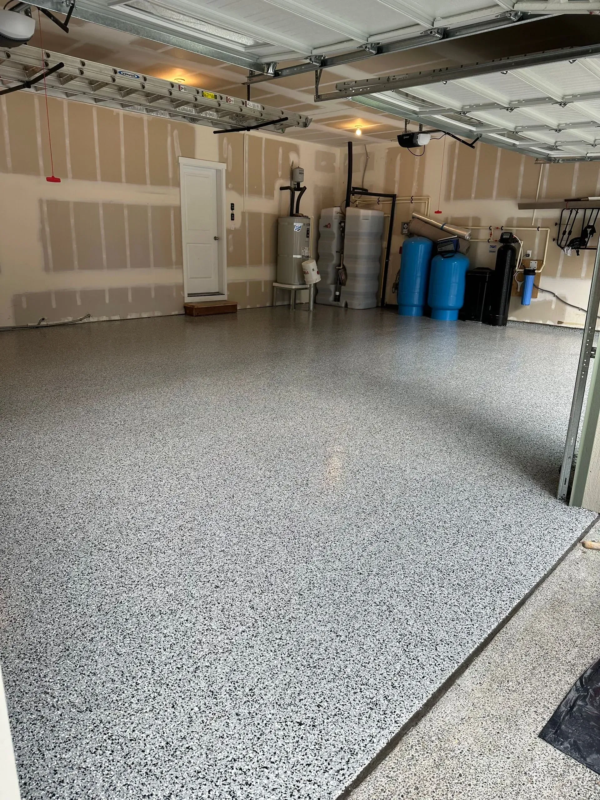 Garage with speckled epoxy floor, unfinished walls, and storage tanks.
