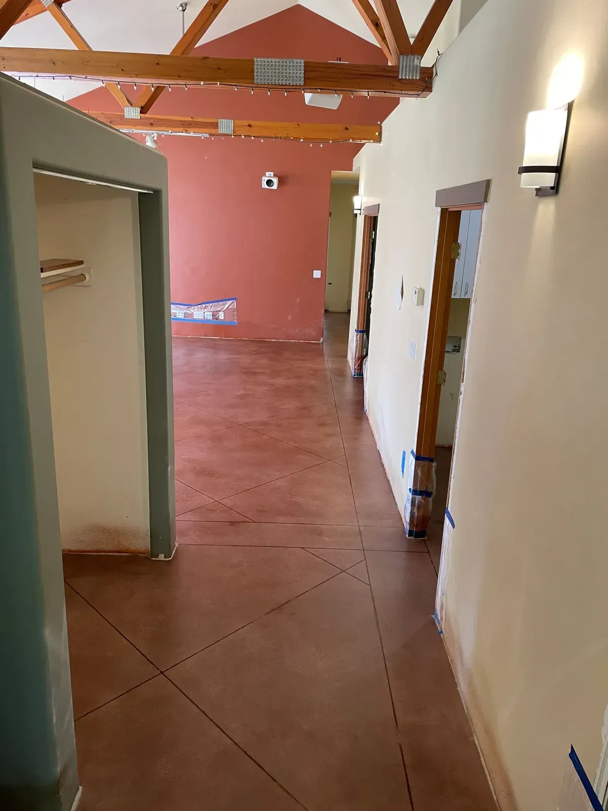 Interior hallway with reddish-brown flooring, tan walls, and wooden door frames.