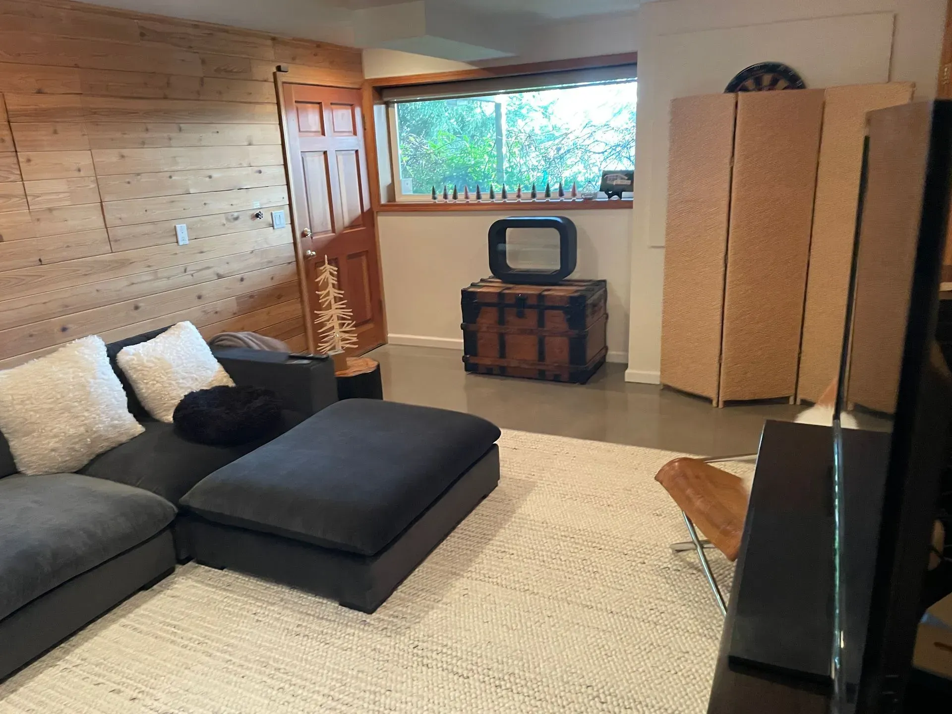 Living room with wood-paneled wall, gray sectional sofa, and a decorative screen.