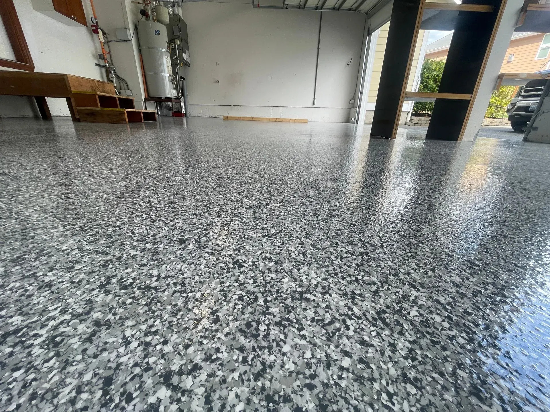 Epoxy-coated garage floor with gray and white chips. Empty garage with sunlight reflecting off the floor.
