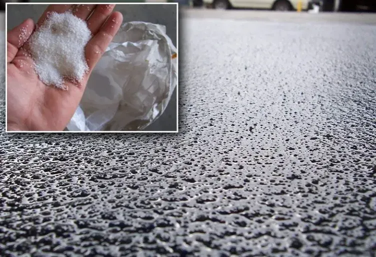 Hand holding white substance, inset on a textured, light gray asphalt surface.
