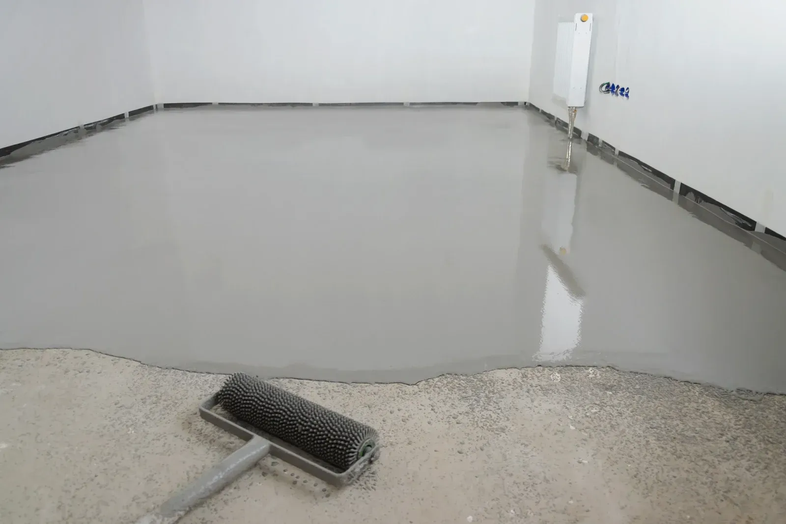 Fresh gray floor coating in a room, with a paint roller in the foreground