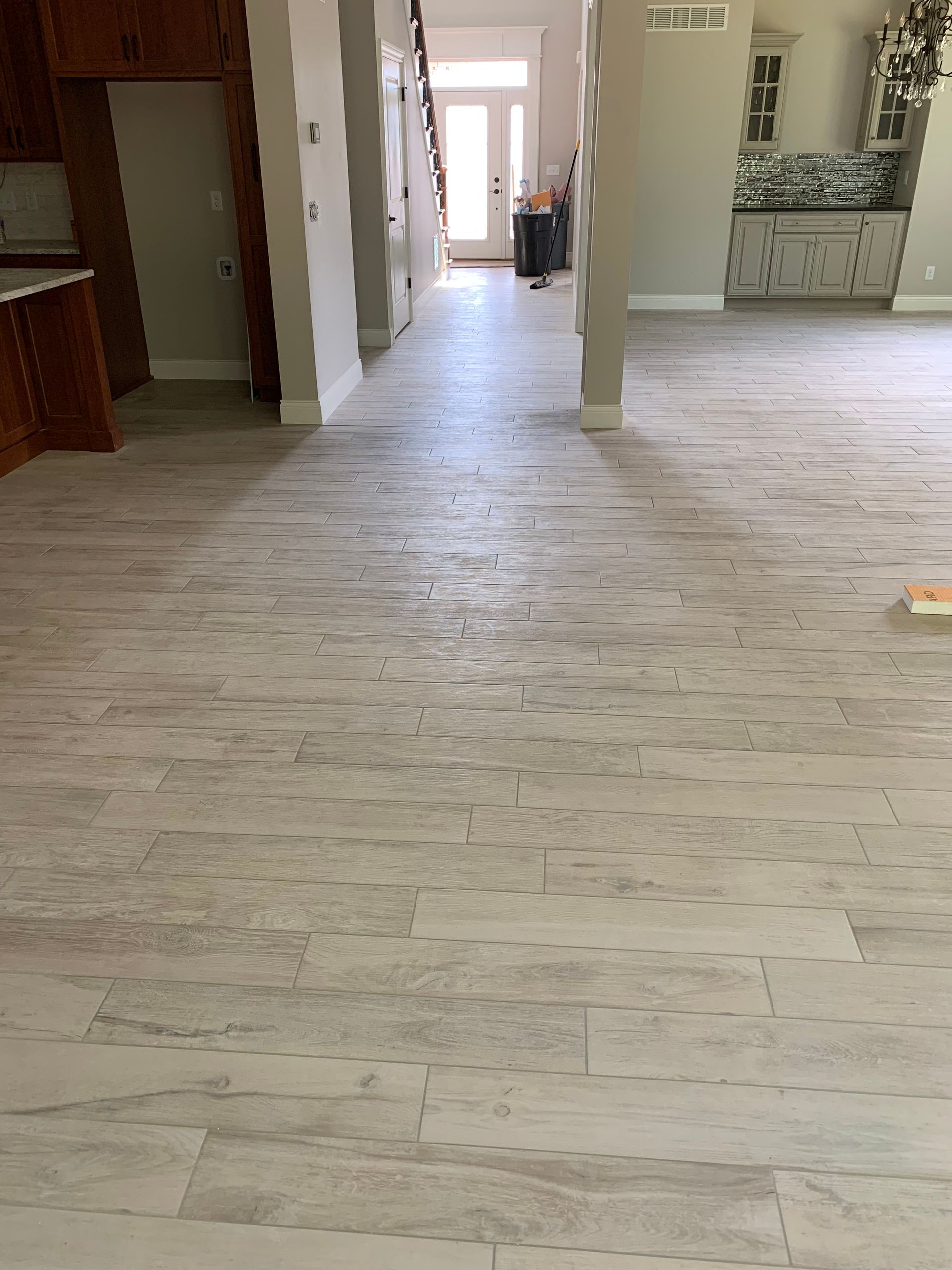 Light gray, wood-look flooring extends down a hallway. A kitchen and stairs are visible at each end.