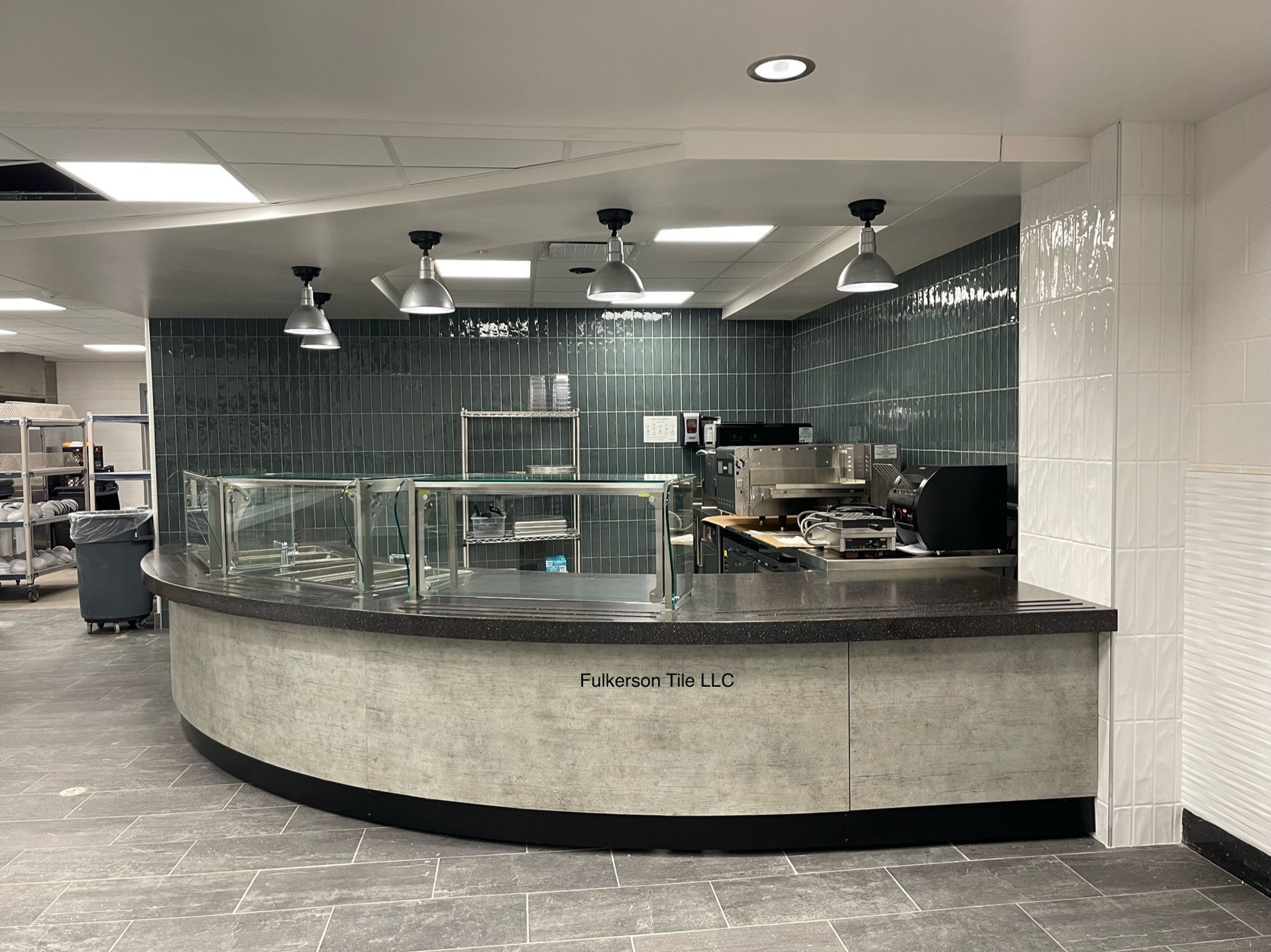 Counter with food serving area, dark countertop, aqua-green tiled wall, stainless steel appliances, black and white floor.