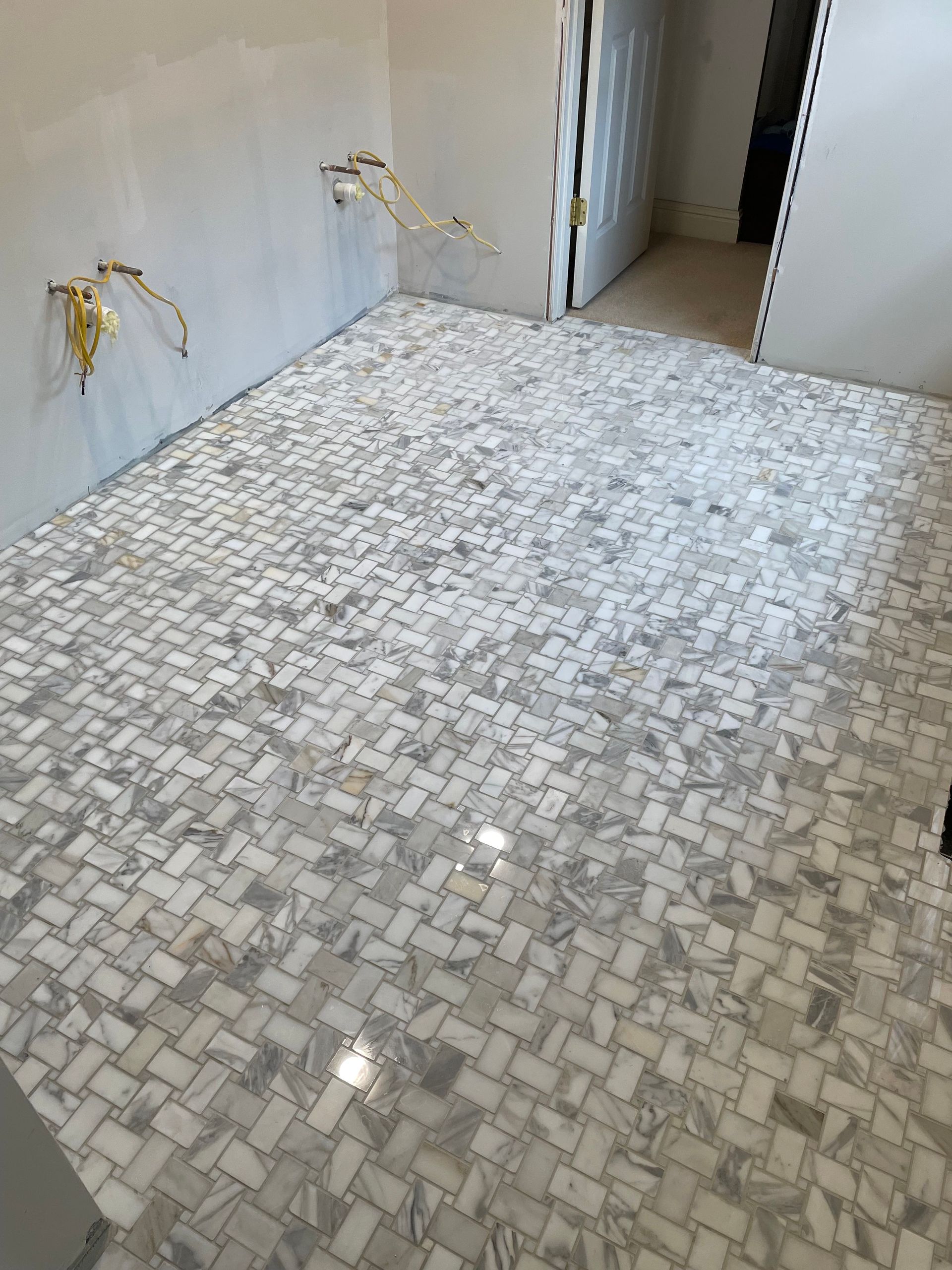 Bathroom with newly installed gray and white patterned tile flooring. Electrical wires from the wall. Doorway in background.
