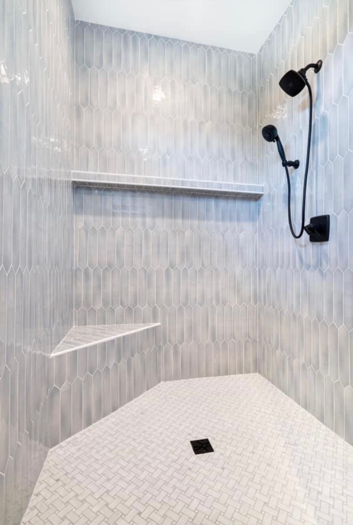 Gray tiled shower with shelves and black shower fixtures.