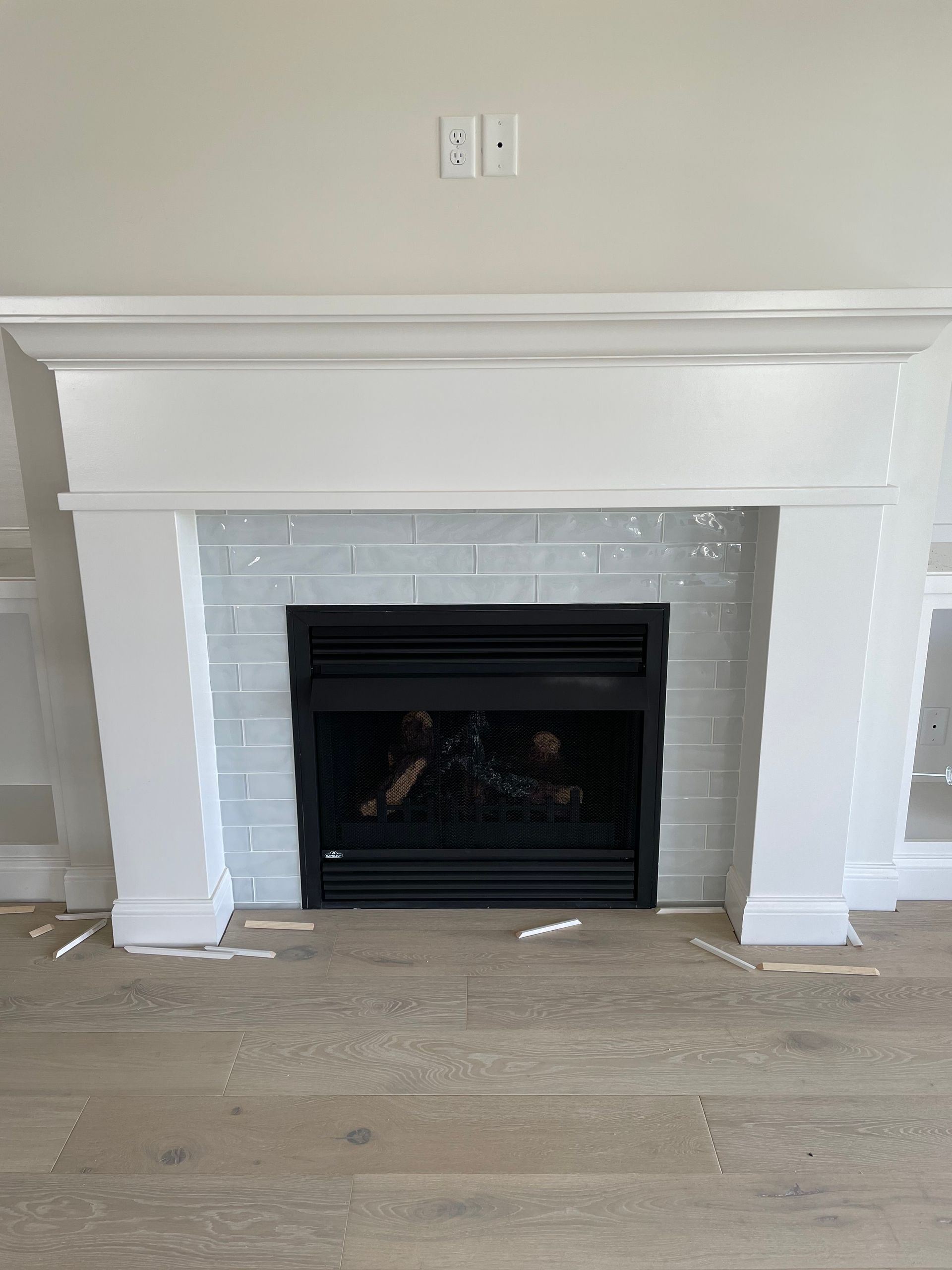 White fireplace with black insert, light blue brick-like tile, and light wood floor.