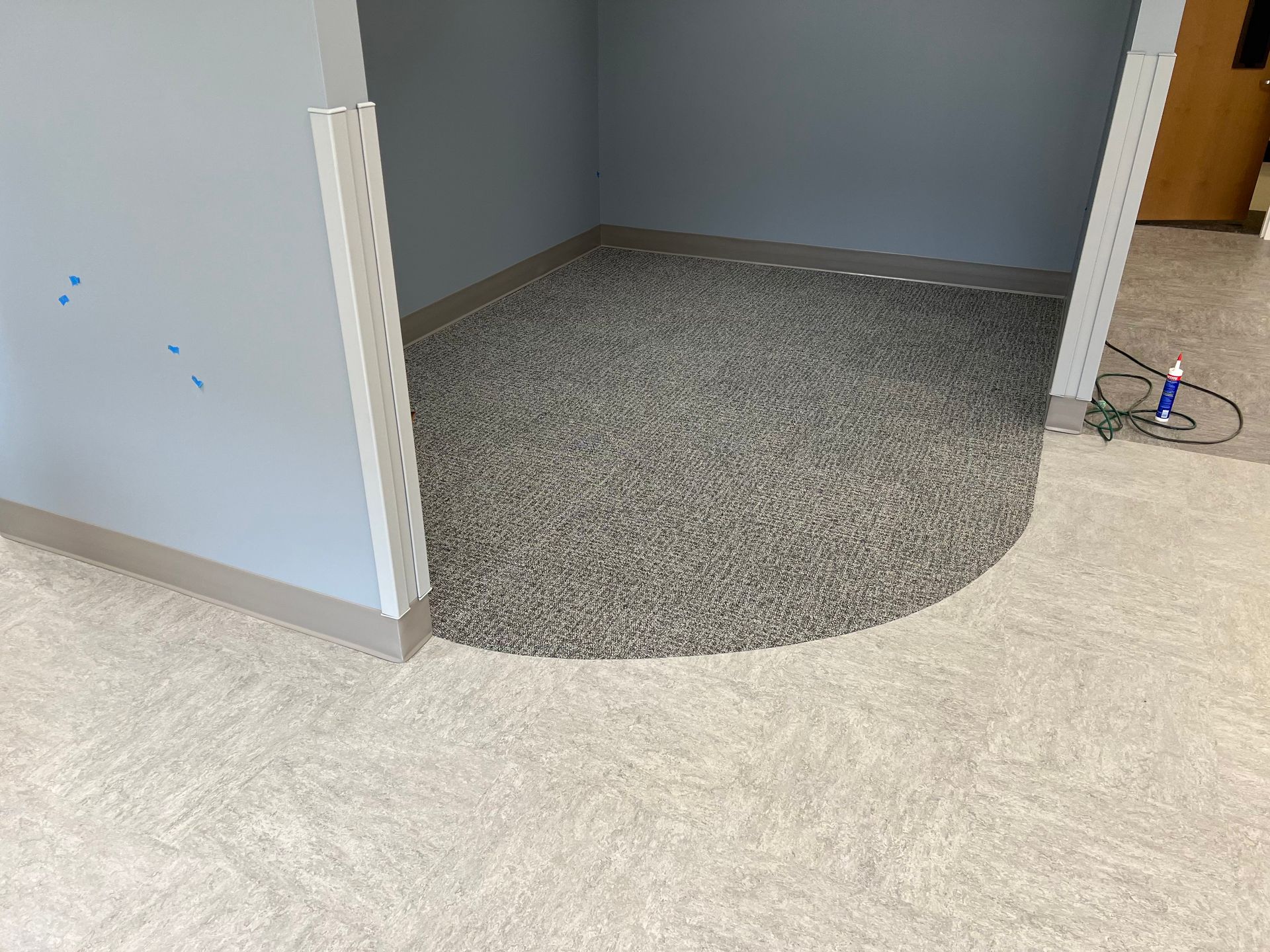 A small alcove with gray aggregate flooring, bordered by light carpet. Blue walls with metal trim.