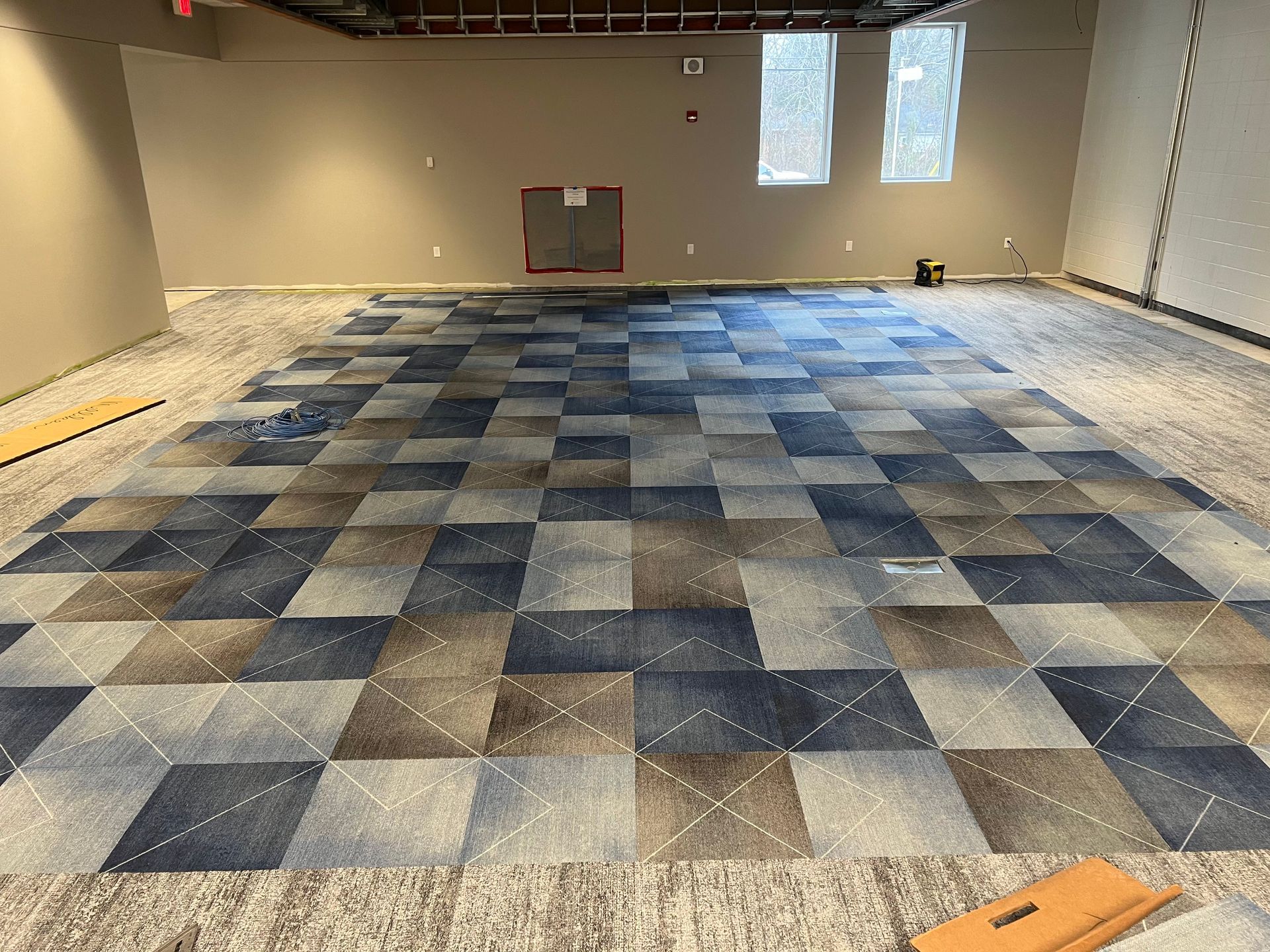 Interior room with checkered blue, gray, and brown carpet being installed. Neutral walls and unfinished ceiling.