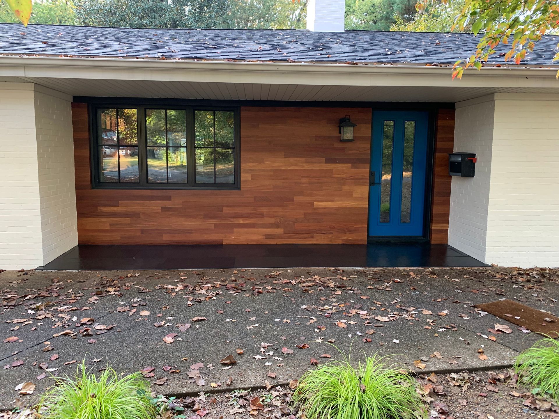 A house exterior with a blue door, wood siding, a black window, and white brick on either side.