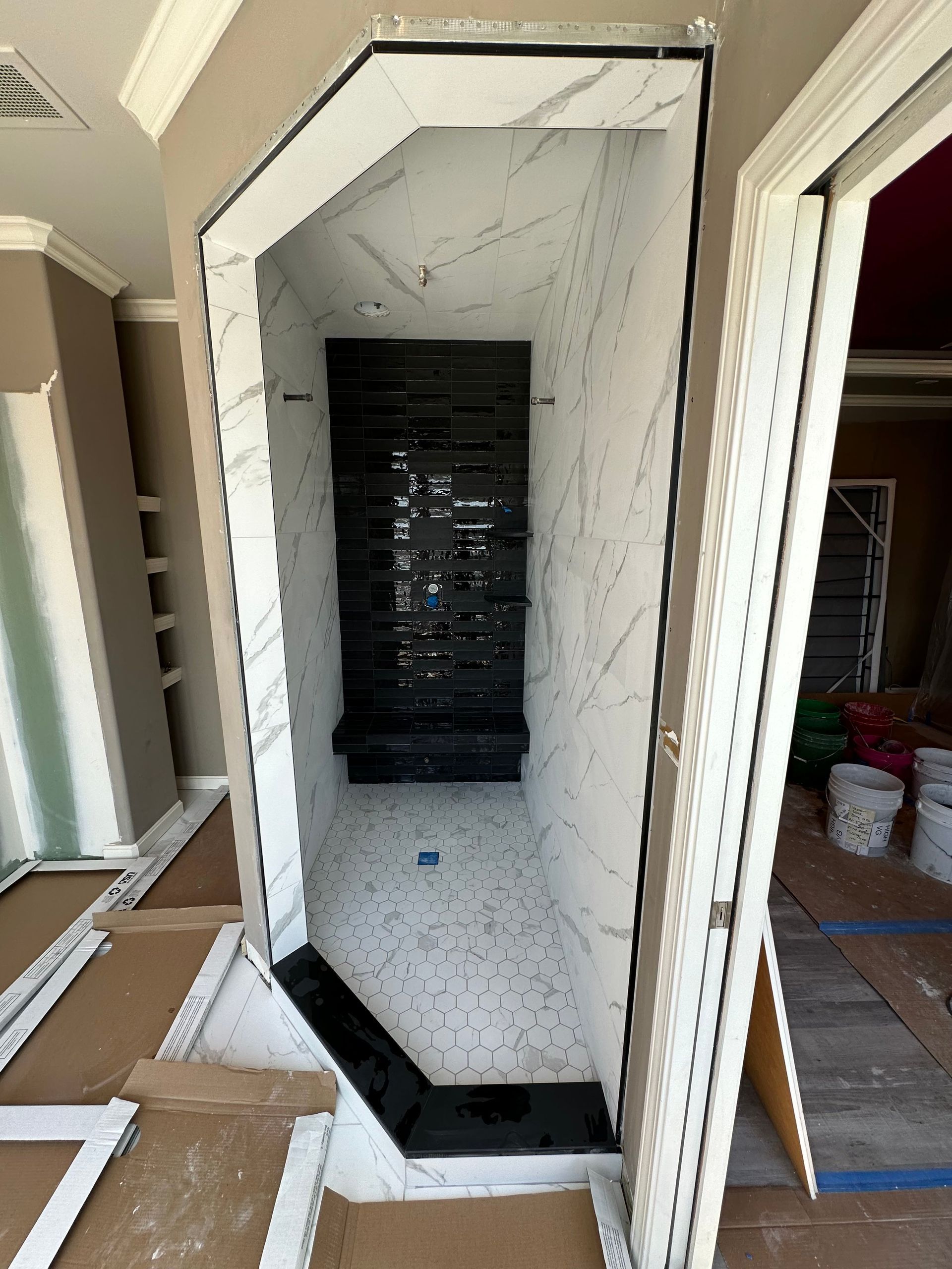 Newly constructed shower with white marble-look tile, black accent wall, and geometric black tiled entrance.