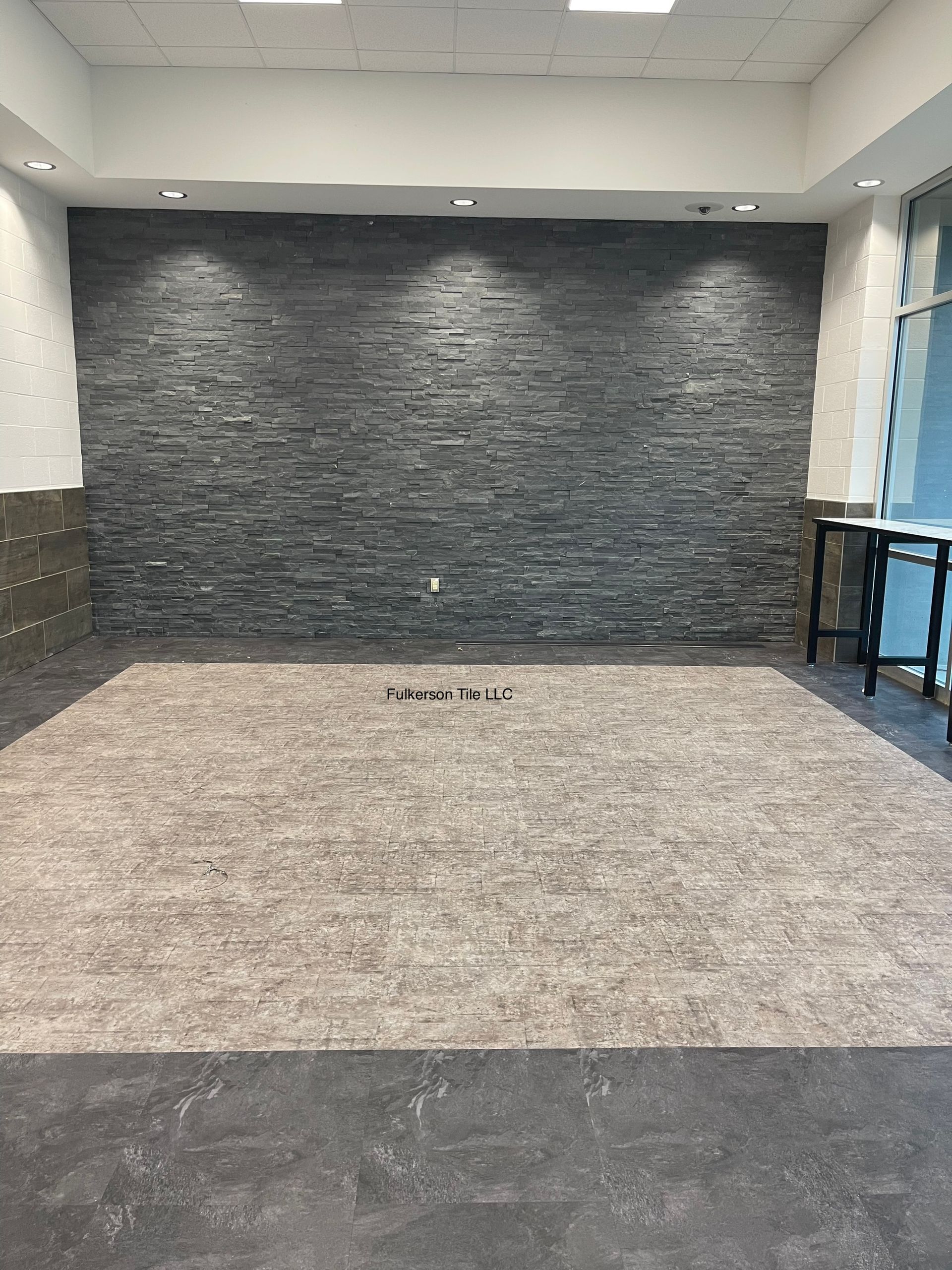 Empty room with gray stone accent wall, light-colored rug, and black tables.