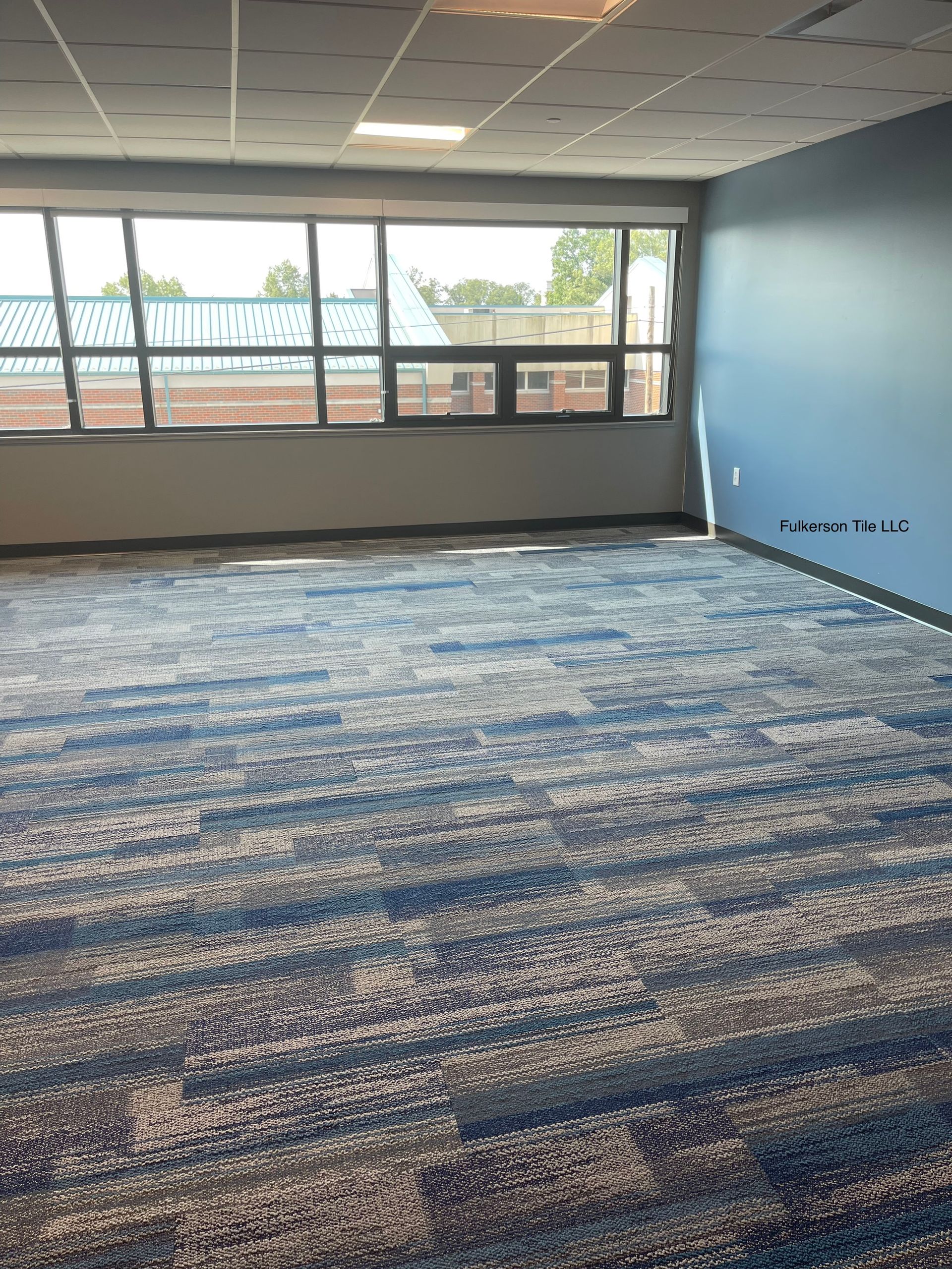 Empty room with patterned blue carpet, large windows, and a blue wall.
