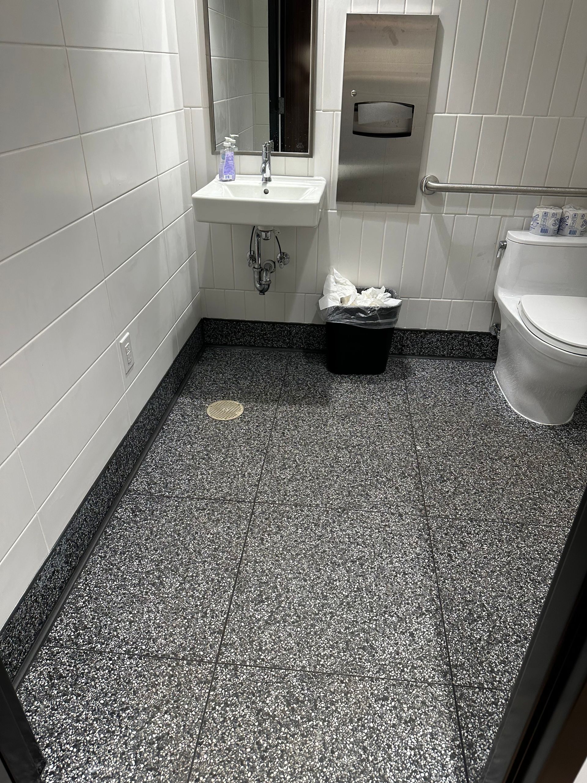 Bathroom with black and gray speckled floor, white walls, and a white toilet.