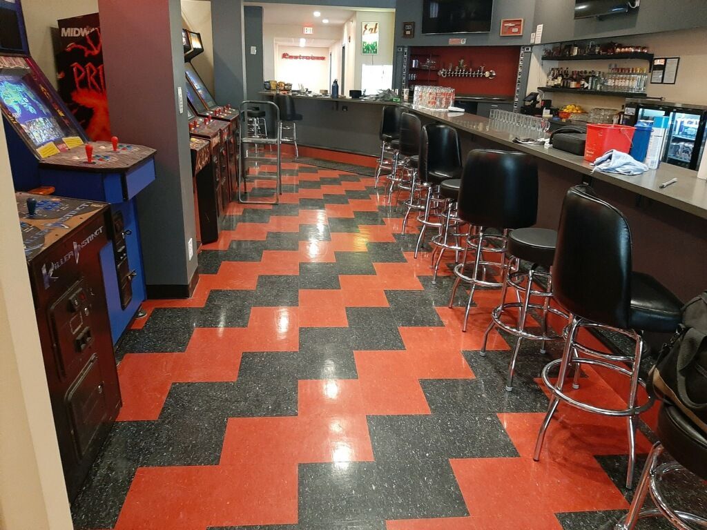 Arcade interior with red and black patterned floor, bar stools, and arcade games.