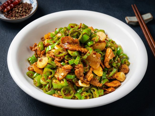 Stir-fried green peppers and sliced meat in a white bowl with chopsticks on a dark table