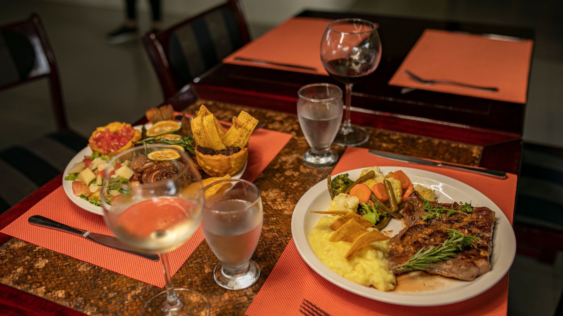 Dos platos principales con bebidas, servidos en una mesa puesta para comer e iluminada con una cálida luz interior.