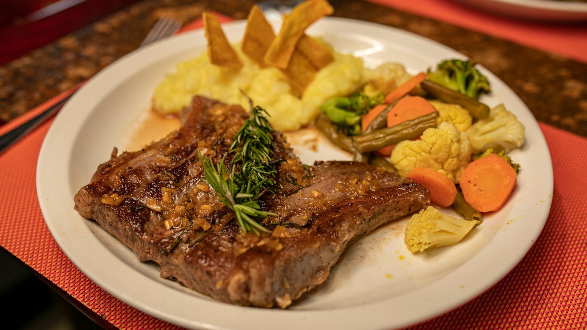 Filete a la parrilla con papas fritas, puré de papas y verduras mixtas en un plato blanco.