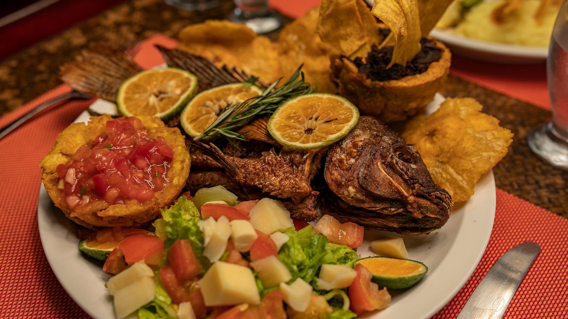 Plato de frituras variadas con rodajas de lima, salsa y ensalada sobre un mantel rojo.
