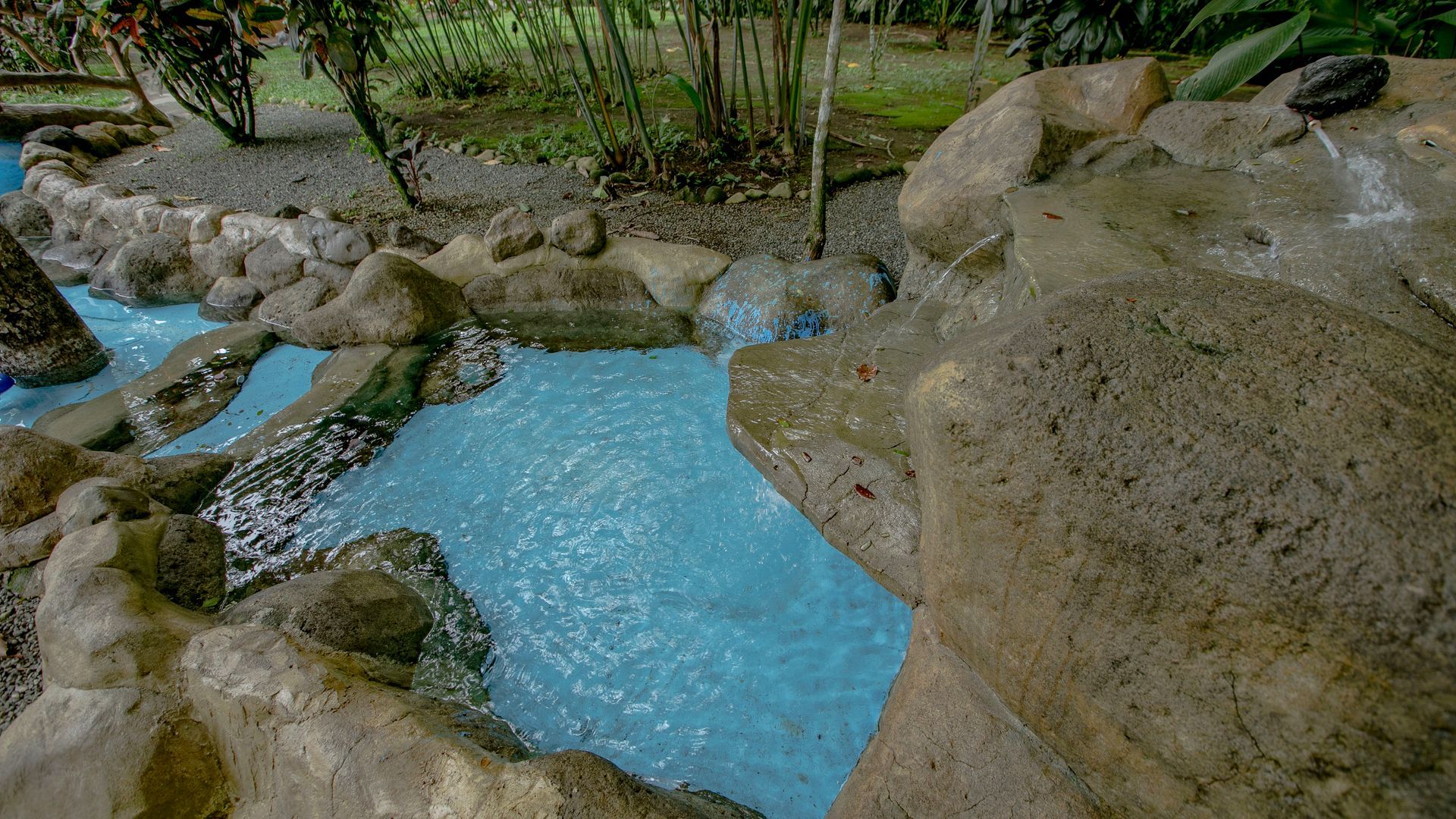 Un arroyo azul fluye a través de un jardín rocoso con exuberante vegetación a su alrededor.