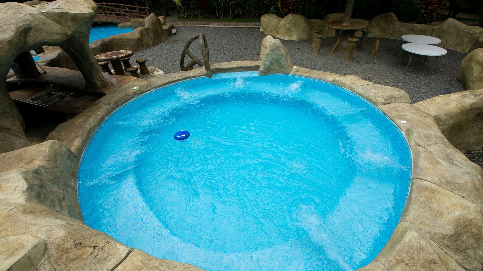 Piscina cubierta azul con bordes que imitan rocas y un pequeño flotador en el agua.