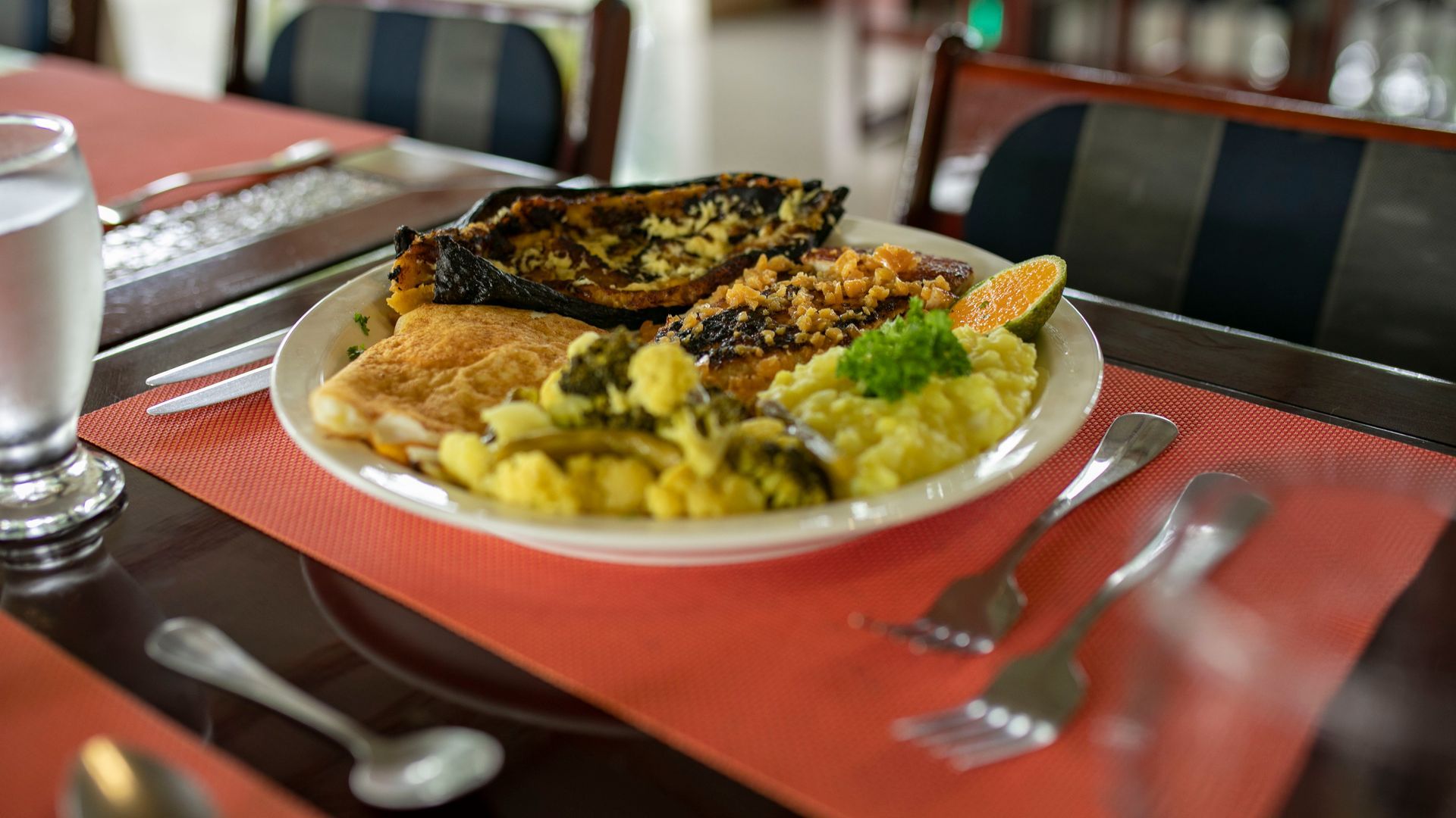 Plato de pescado a la parrilla con arroz y verduras sobre un mantel individual rojo en una mesa de restaurante.