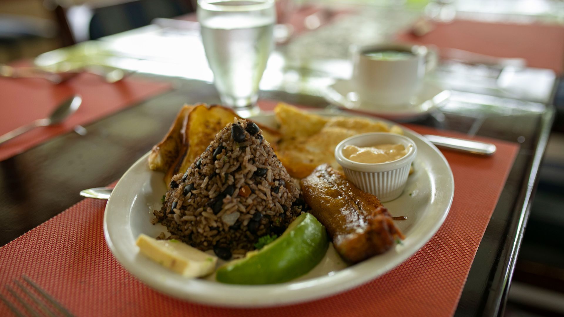 Plato gourmet con carne a la parrilla, arroz, lima y salsa sobre un mantel individual rojo en una mesa.
