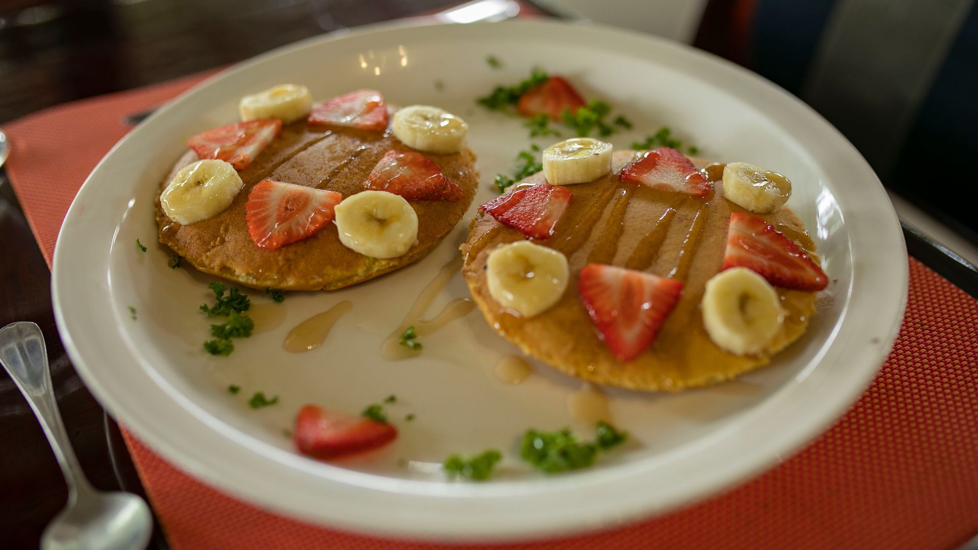 Dos panqueques con fruta sobre un plato blanco, adornados con rodajas de plátano y fresas.