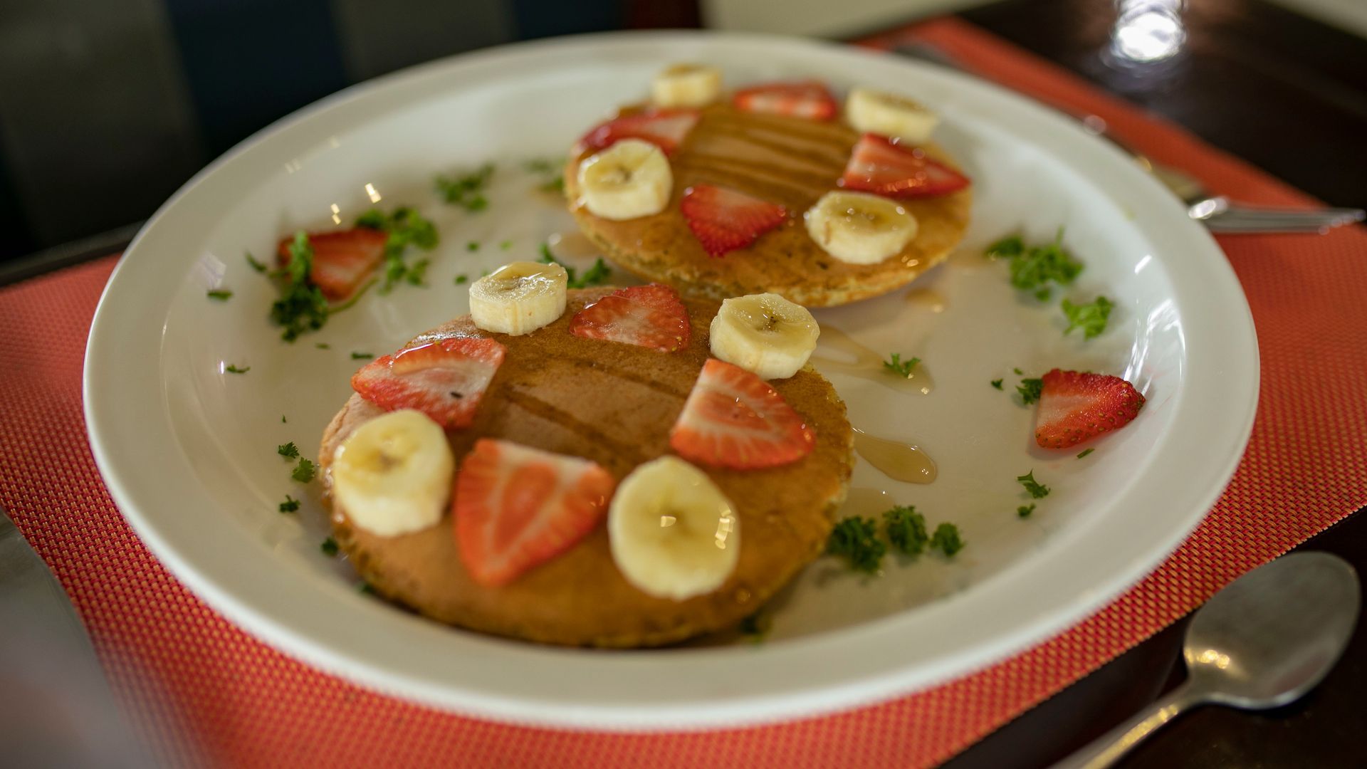 Plato de filete de salmón cubierto con fresas y plátano en rodajas, adornado con hierbas sobre un mantel individual rojo.