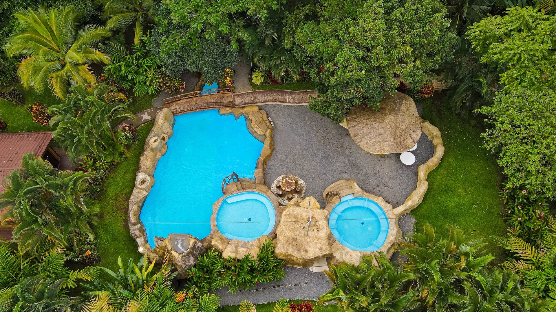 Vista aérea de una zona de piscinas tropicales con tres piscinas azules rodeadas de rocas y exuberante vegetación.