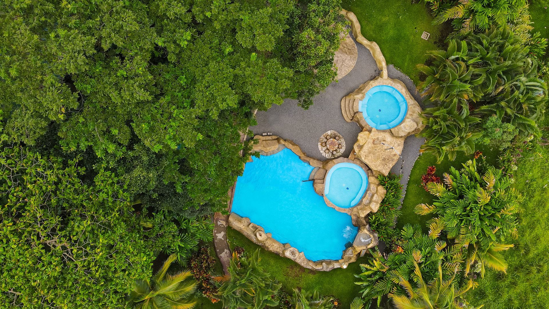 Vista aérea de dos piscinas de un azul brillante, rodeadas de una densa vegetación tropical y senderos de piedra.