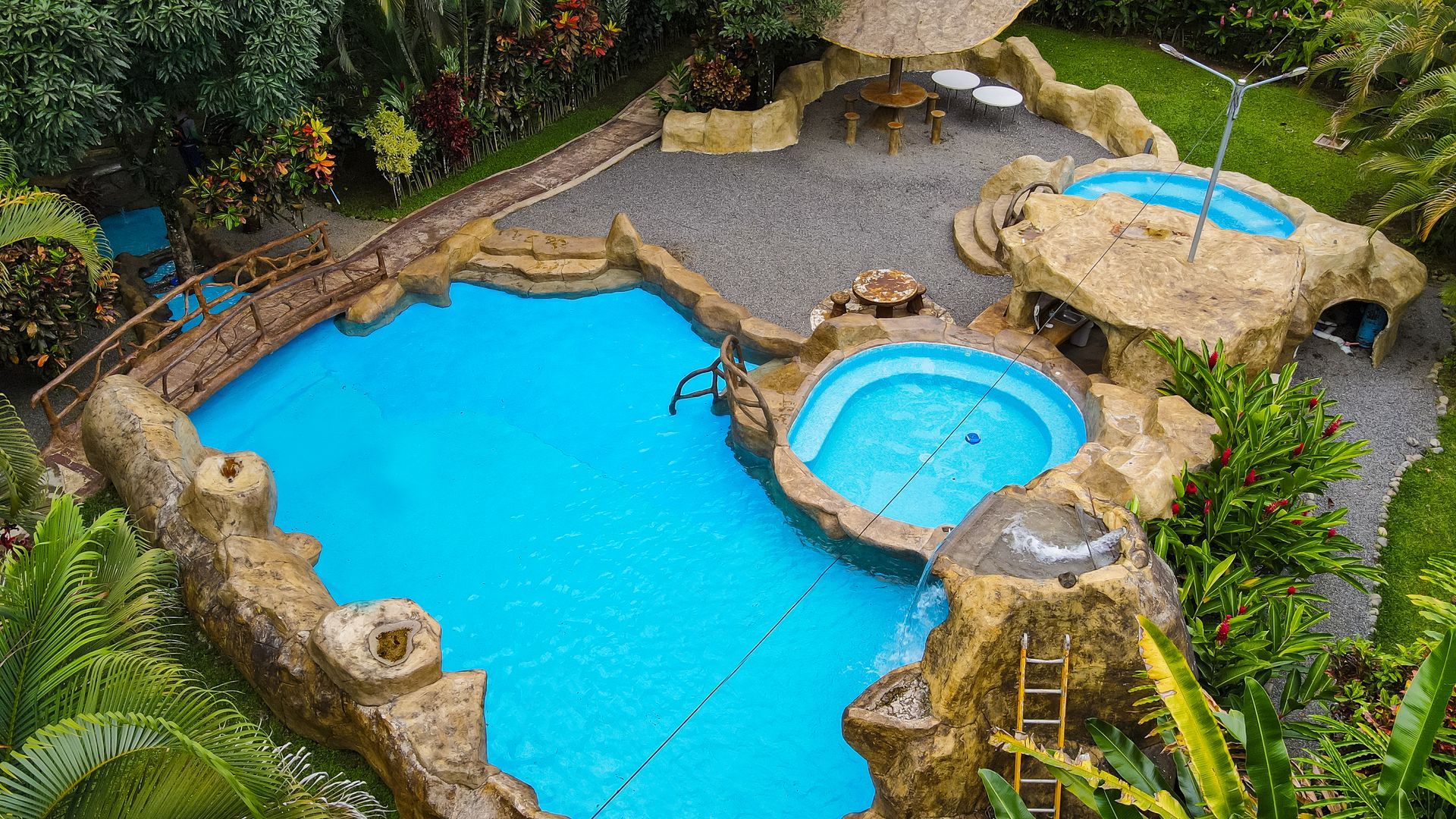 Patio trasero con una gran piscina turquesa, un pequeño jacuzzi y un paisaje de rocas naturales.