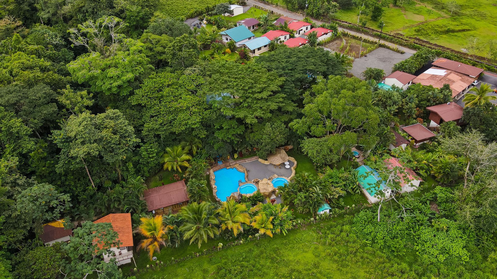 Vista aérea de un complejo turístico tropical con piscinas azules y villas en medio de densos árboles verdes.